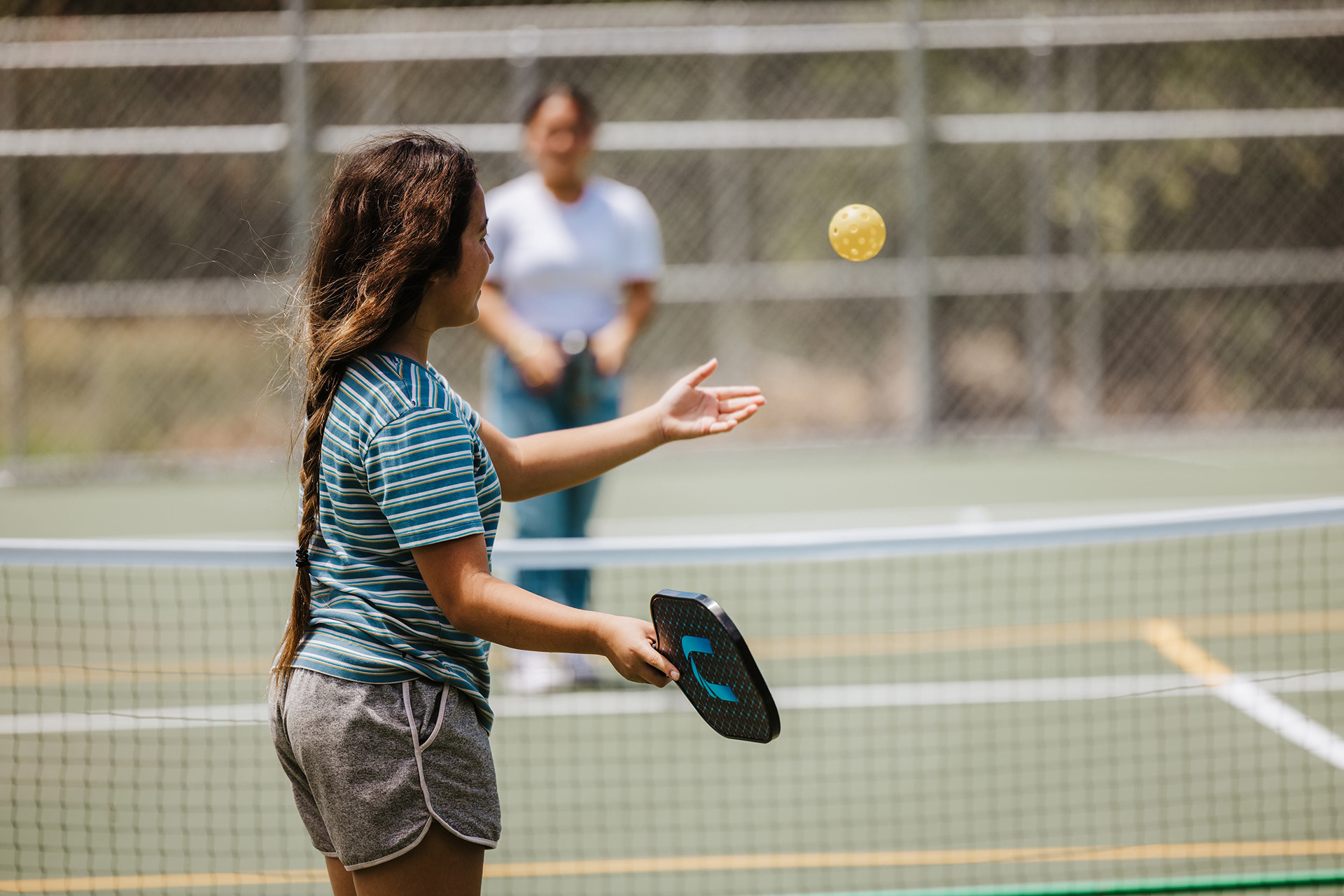 Two girls play pickleball on a sunny day.